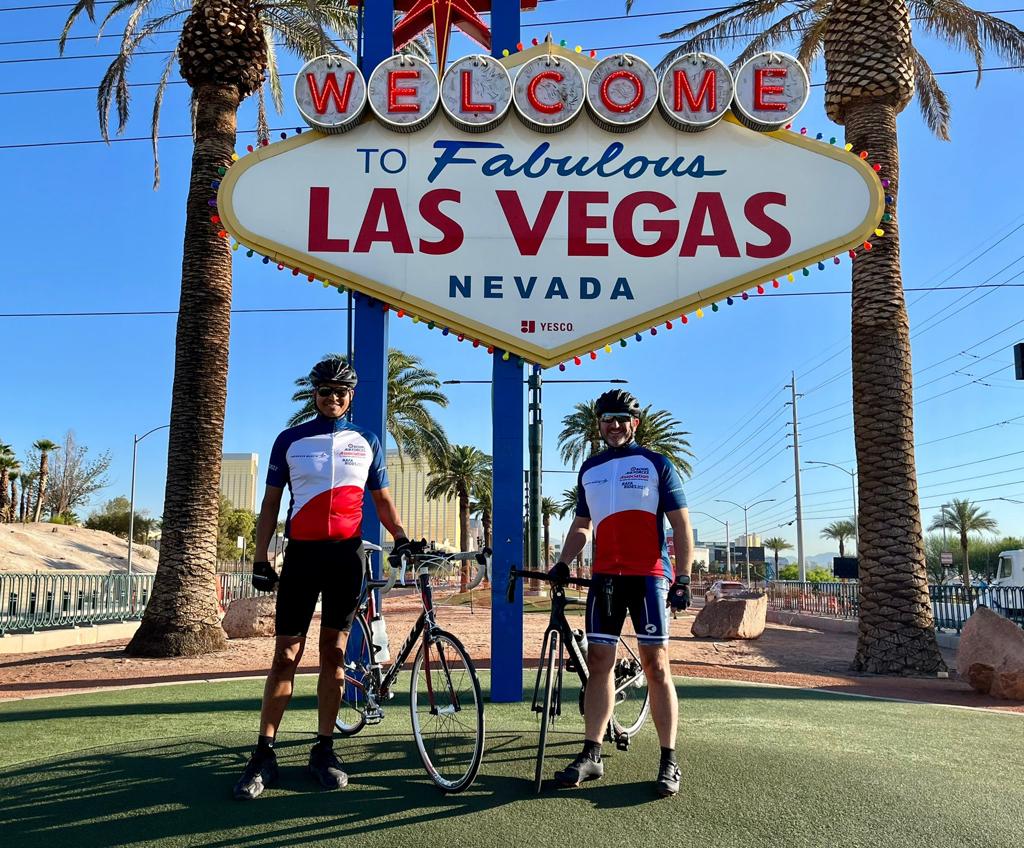 RAF Association members stand with bikes under Las Vegas sign and palm trees.